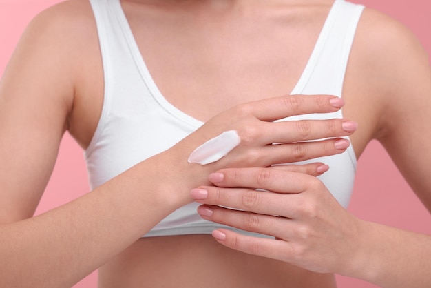 Woman with smear of body cream on her hand against pink background closeup