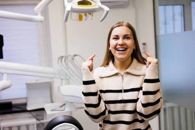 Una donna con un sorriso sul viso con parentesi graffe sui denti sta aspettando nello studio dentistico il suo medico. gabinetto in una moderna clinica odontoiatrica