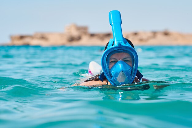 青い海でダイビングシュノーケルフルフェイスマスクを持つ女性