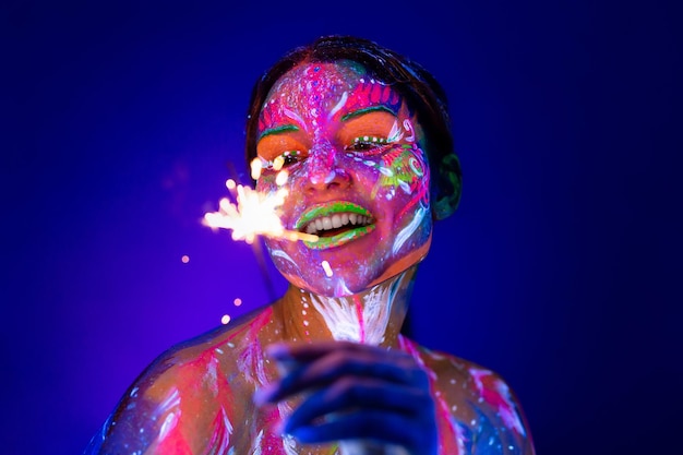 Женщина с бенгальским огнем в неоновом свете Красивая девушка-модель красочный яркий флуоресцентный макияж