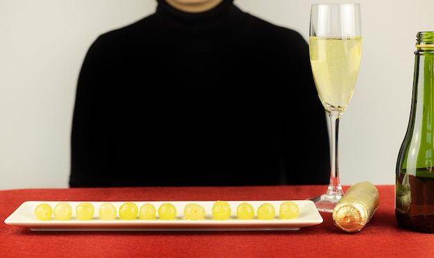 Woman with sparkler next to New Year's grapes on plate and glass of champagne