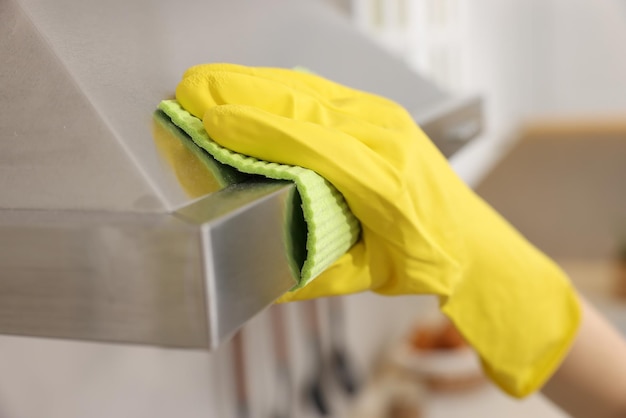 Woman with spray bottle and microfiber cloth cleaning kitchen hood indoors closeup