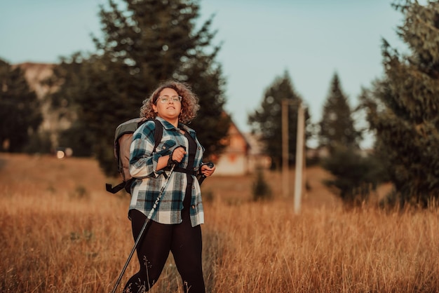 A woman with sticks a backpack on her back and mountaineering equipment walking on top of a mountain at sunset