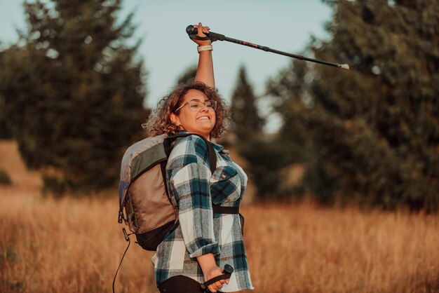 A woman with sticks a backpack on her back and mountaineering equipment walking on top of a mountain at sunset