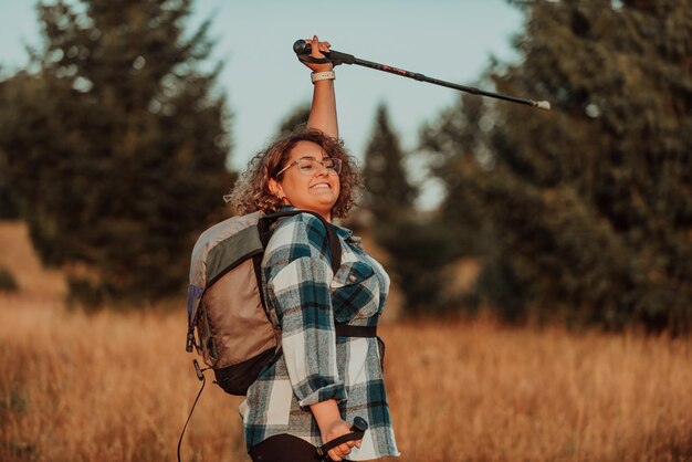 Una donna con bastoni uno zaino sulla schiena e attrezzatura da alpinismo che cammina sulla cima di una montagna al tramonto