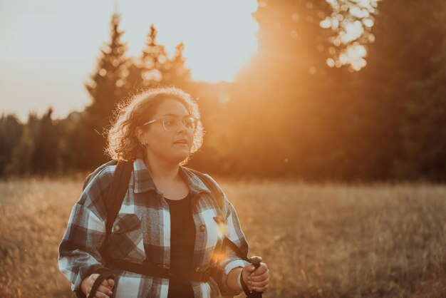 A woman with sticks a backpack on her back and mountaineering equipment walking on top of a mountain at sunset