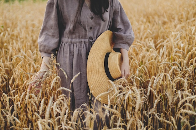 Woman with straw hat holding wheat stems in field cropped view Summer countryside Rural slow life