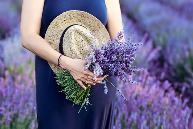 夏のラベンダー畑で彼女の手に麦わら帽子とラベンダーの花束を持つ女性。