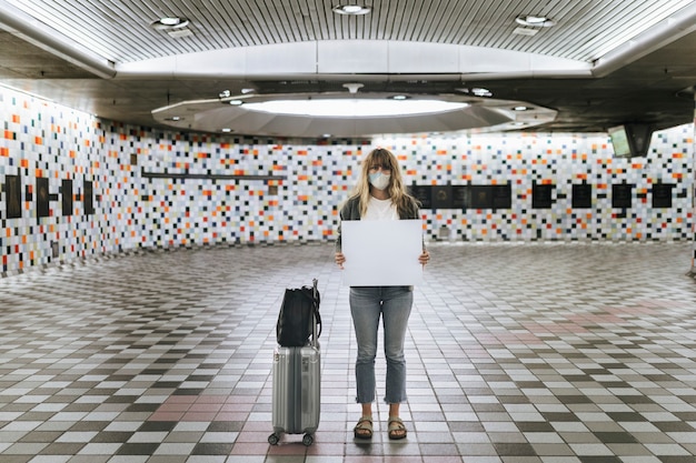 Woman with a suitcase holding a blank paper during the coronavirus outbreak