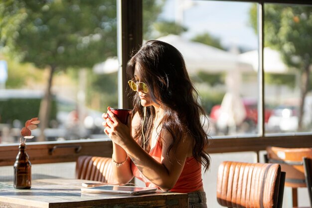 写真 コーヒーショップでリラックスしながらコーヒーを飲むサングラスをかけた女性