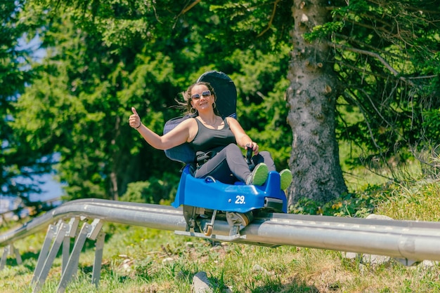 Woman with sunglasses rides a mountain roller coaster with a thumbs up Warm summer day on the mountain