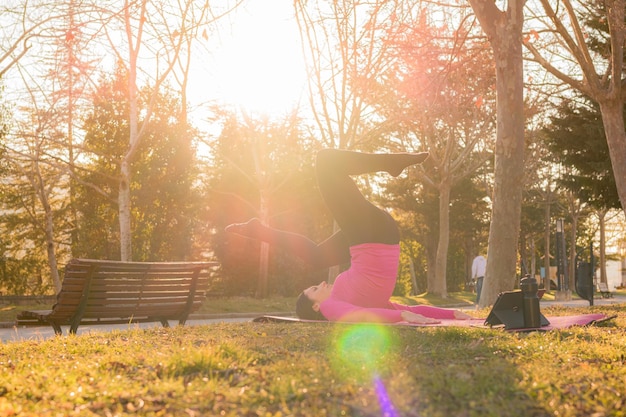 Donna con un tablet che esegue esercizi di yoga in un parco al tramonto