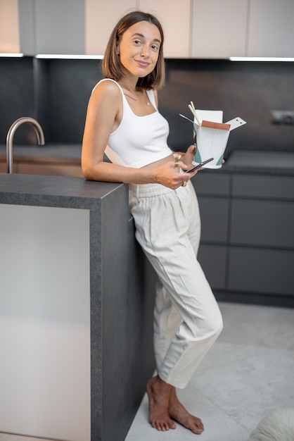 Woman with takeaway food and phone at kitchen