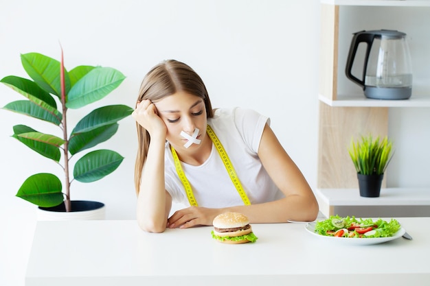 Woman with a taped mouth sits at a table with fast food