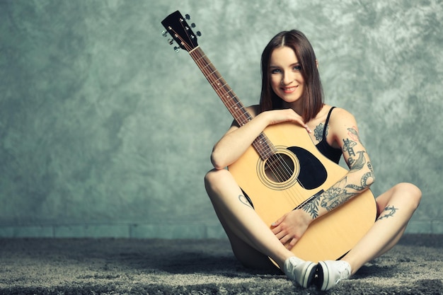 Woman with tattoo and guitar sitting on grey background