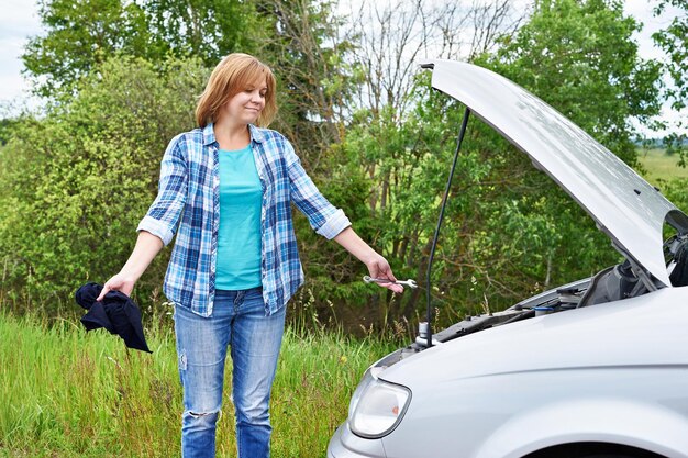 壊れた車の近くで道具を持つ女性