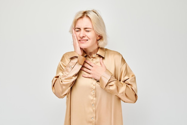 Woman with toothache touching cheek feeling pain on a gray background