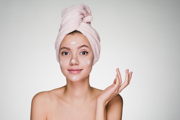 Woman with towel on her head after shower applied cream on face skin