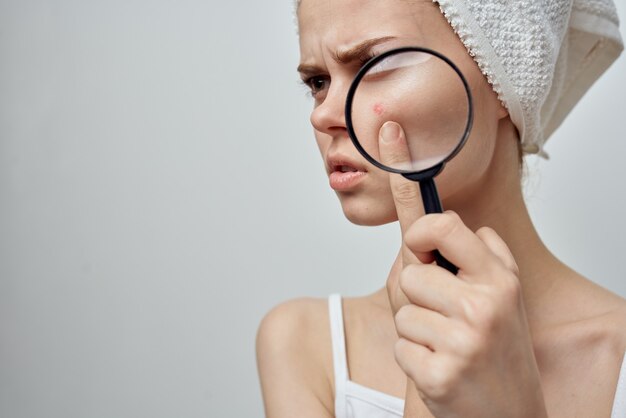 Woman with a towel on her head holds a magnifying glass near\
face