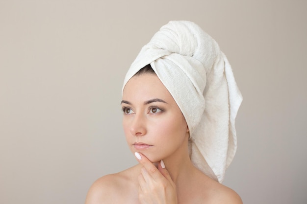 woman with towel wrapped around her head looking up thoughtfully touching her chin with her finger