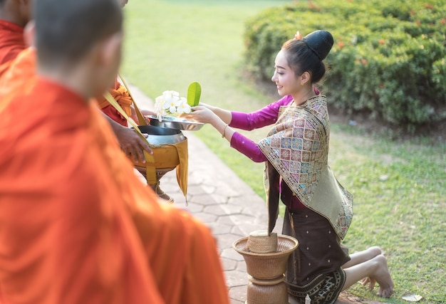 Woman with traditional dress sit pray respect monk, present Buddhism people Make merit with monk that representative of Buddha. Woman Make merit by offering food to monk.
