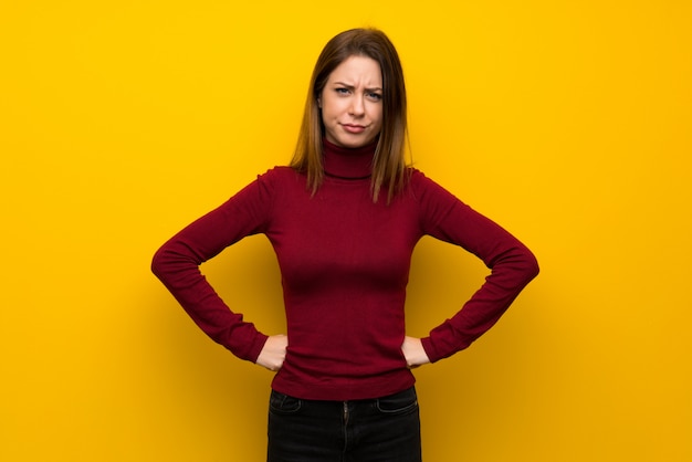 Woman with turtleneck over yellow wall angry