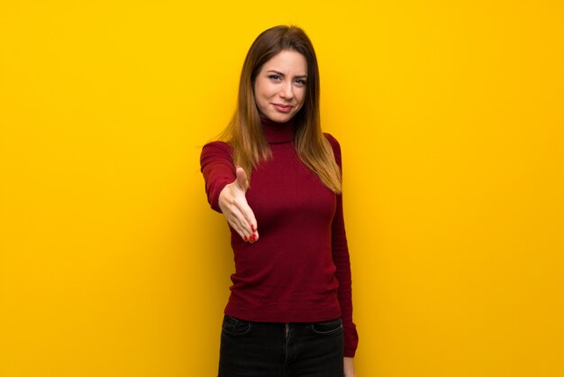 Woman with turtleneck over yellow wall shaking hands for closing a good deal