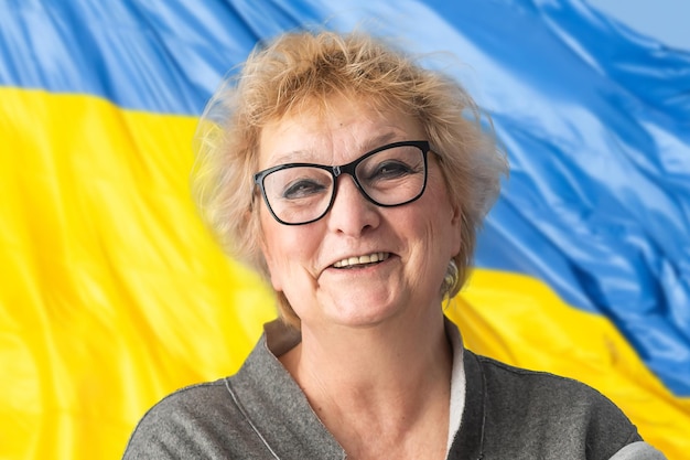 Woman with Ukraine flag at background looking at camera Concept of standing with Ukrainian nation in war with Russia