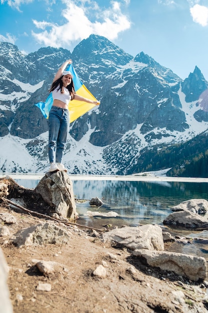 A woman with Ukrainian flag is standing on the shore of a lake Morskie Oko