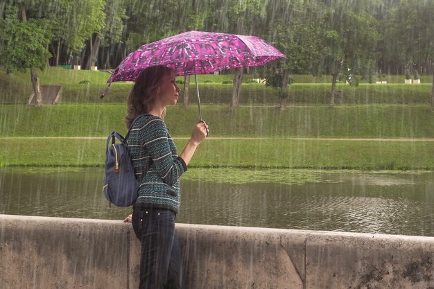 夏の雨の中で自然の中で傘を持つ女性