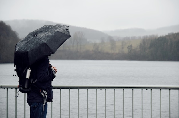 写真 雨季に湖のそばに立っている傘をかぶった女性