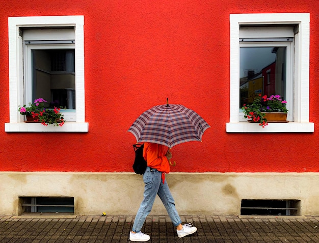 Foto donna con l'ombrello che cammina contro la casa