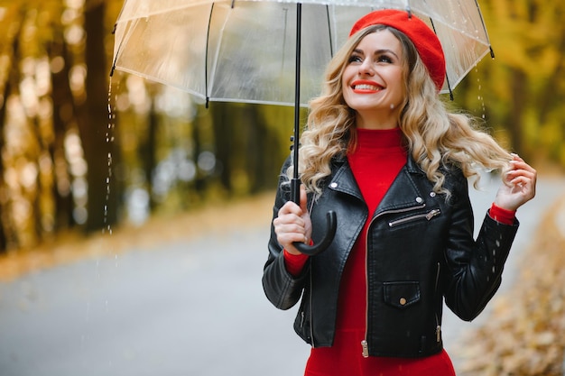 美しい秋の公園で雨の中歩いている傘を持つ女性