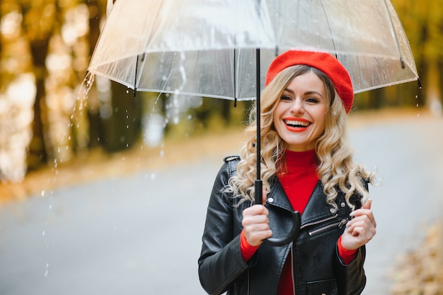 美しい秋の公園で雨の中を歩く傘を持つ女性。