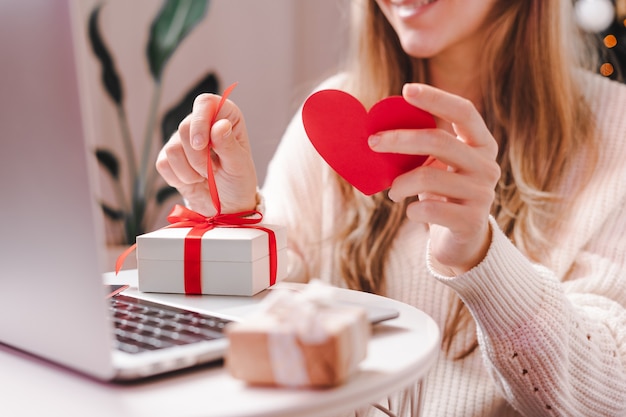 Woman with Valentine card and gift having a video chat on laptop