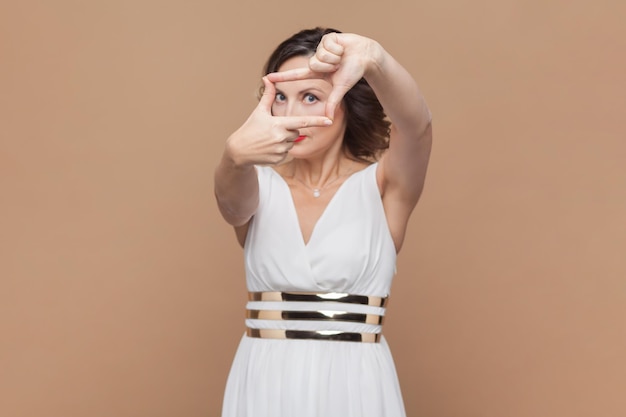 Woman with wavy hair makes frame gesture over head searches perfect angle makes picture