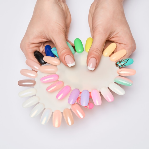 Woman with well-groomed hands and healthy nails holding palette with swatches collection of nail Polish for manicure.