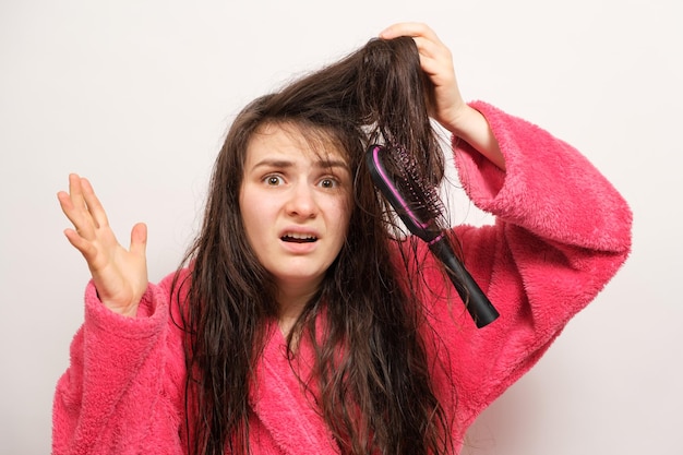 Женщина с мокрыми длинными запутанными волосами пытается расчесаться
