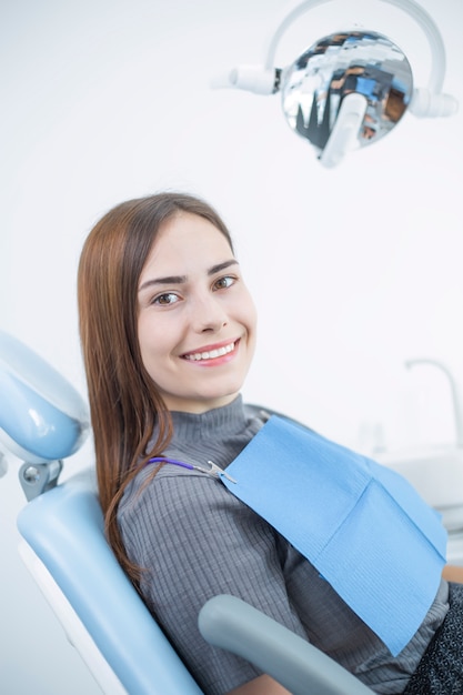 A woman with white teeth and a beautiful smile sits on a dental chair.