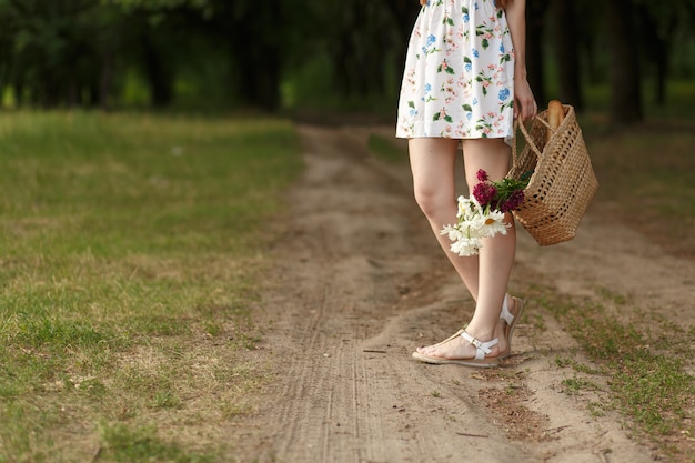 Woman with a wicker basket and flowers on a country road.