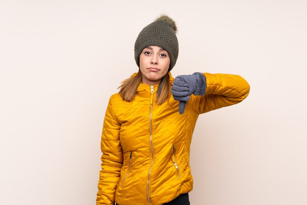 La donna con il cappello dell'inverno sopra la parete isolata che mostra il pollice giù firma