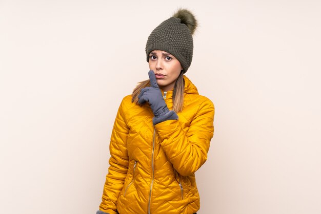 Woman with winter hat over wall doing silence gesture