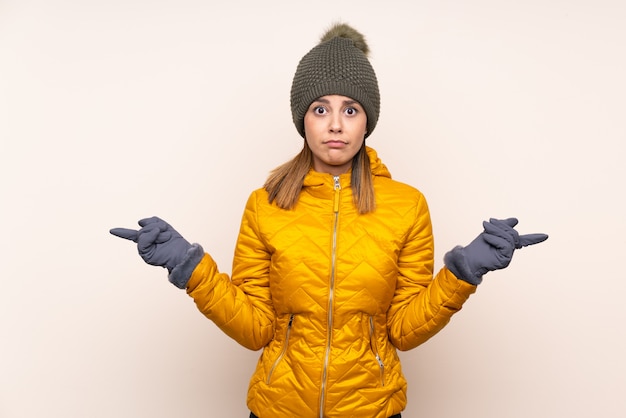 Woman with winter hat over wall pointing to the laterals having doubts