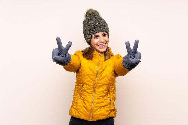 Woman with winter hat over wall smiling and showing victory sign