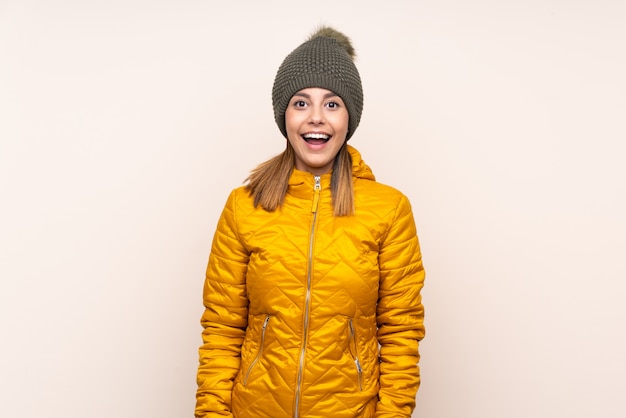 Woman with winter hat over wall with surprised facial expression