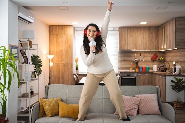 Woman with wireless headphones on sofa singing karaoke at home