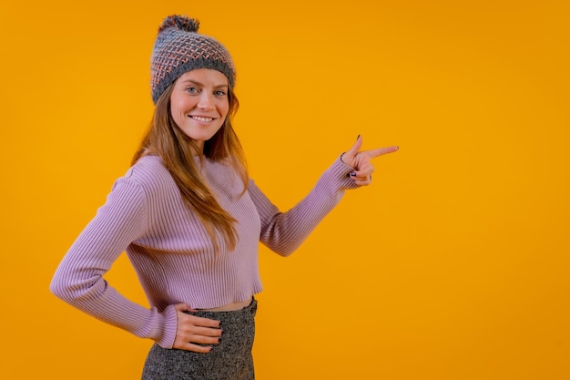 Woman with wool cap on a yellow background pointing to the right copy paste advertising concept