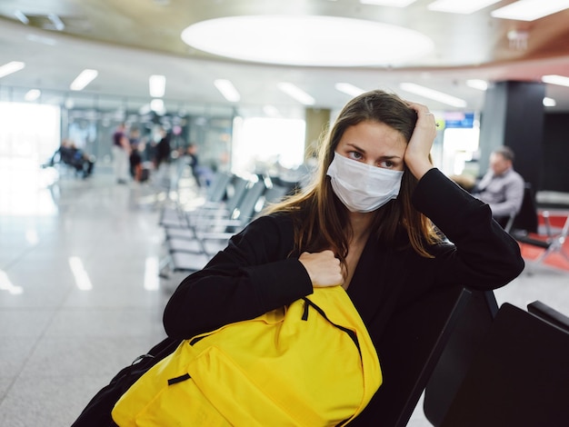 Woman with yellow backpack in medical mask waiting for flight