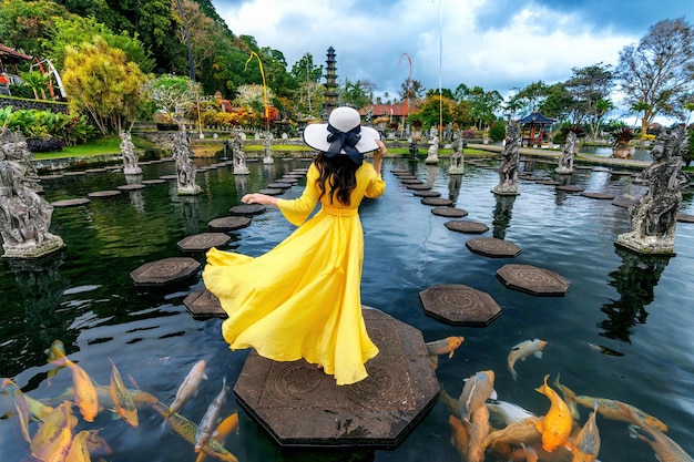 バリ島のティルタガンガ水の宮殿の池に立つ黄色いドレスを着た女性、色とりどりの魚