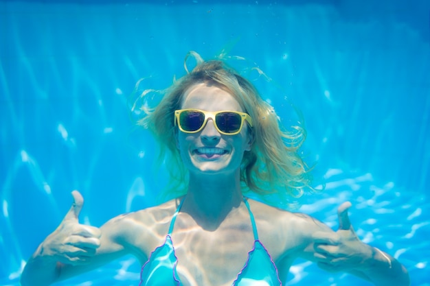 スイミングプール内の水の下で黄色のサングラスをかけた女性